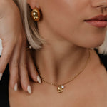 Kullattu kaulakoru nuoren naisen päällä. Minimalistinen kaulakoru jossa yksi helmi.