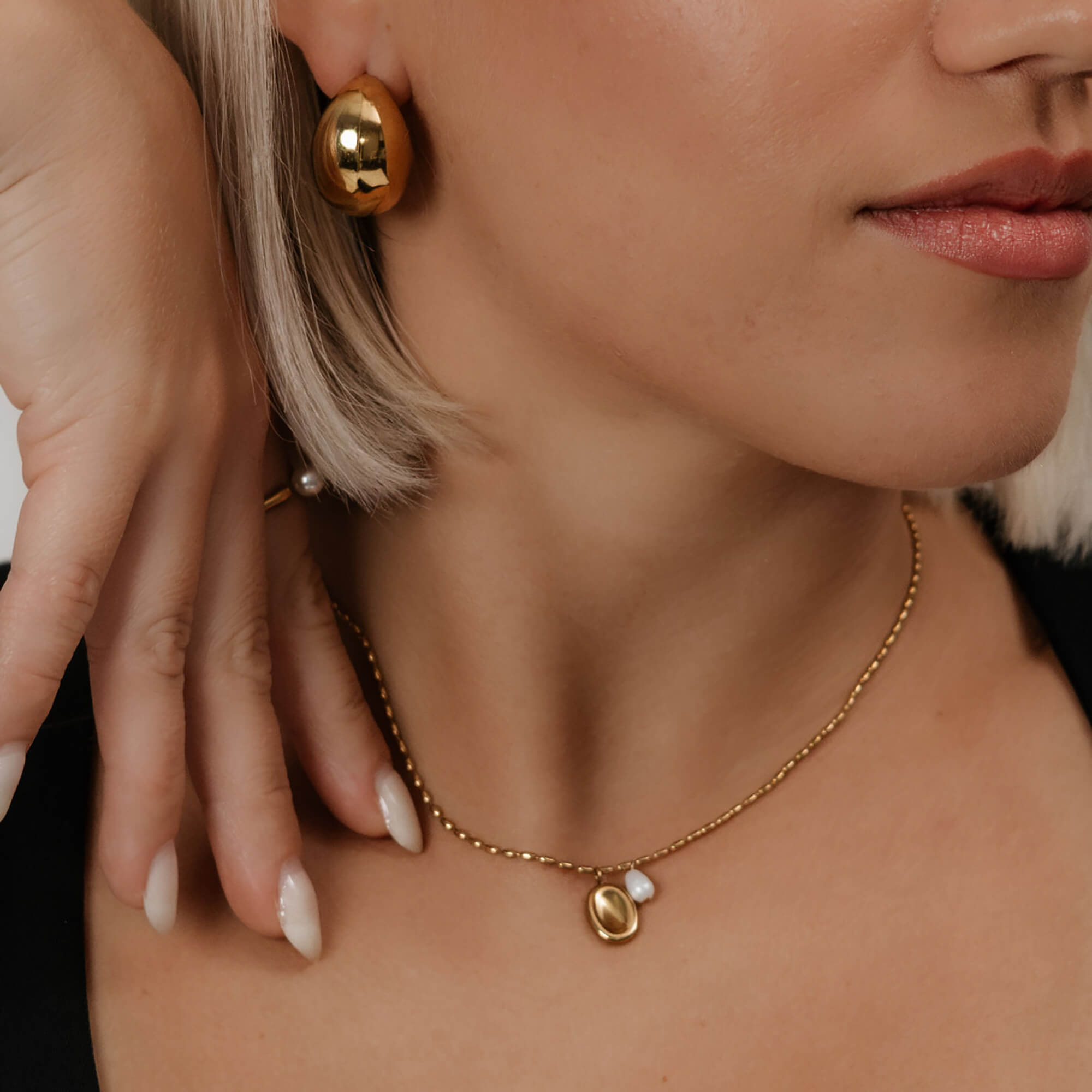 Kullattu kaulakoru nuoren naisen päällä. Minimalistinen kaulakoru jossa yksi helmi.
