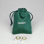 Helmikorvakorut satiinipussin edessä