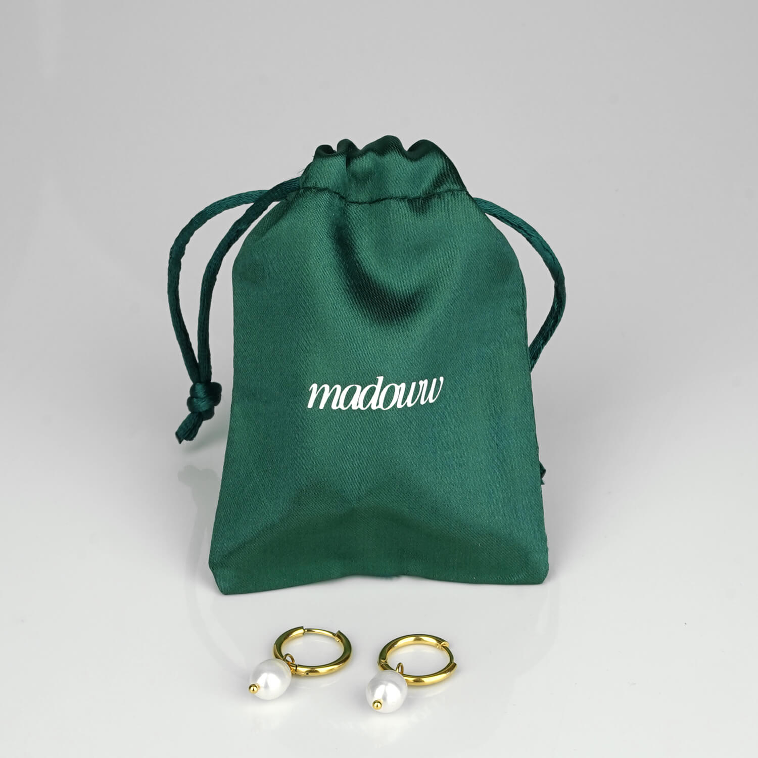 Helmikorvakorut satiinipussin edessä