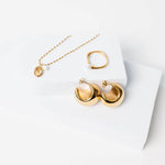 Kullattu sormus jossa koristeena helmi valkoista taustaa vasten. Kuvassa myös kullatut korvikset ja kullattu kaulakoru.