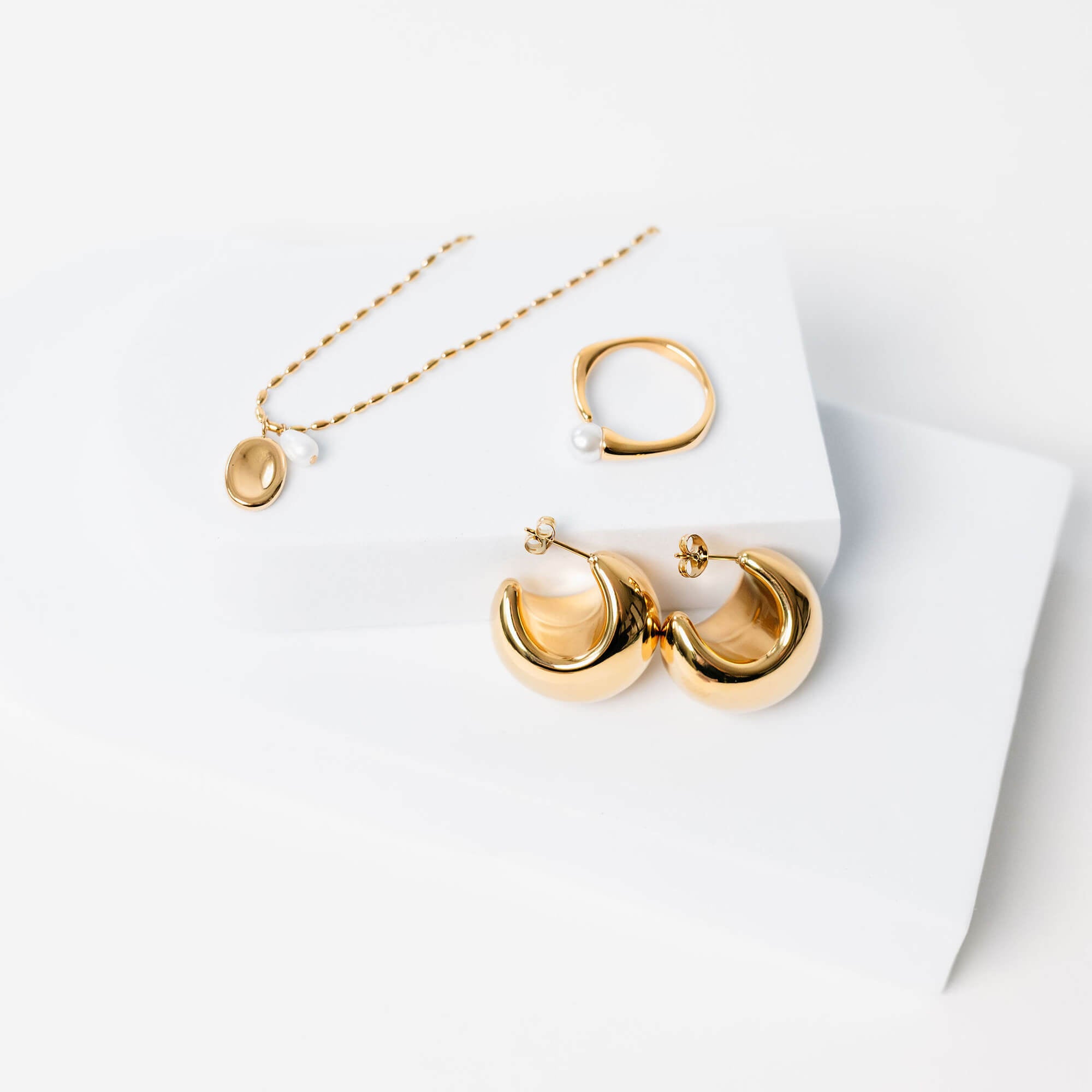 Kullattu sormus jossa koristeena helmi valkoista taustaa vasten. Kuvassa myös kullatut korvikset ja kullattu kaulakoru.