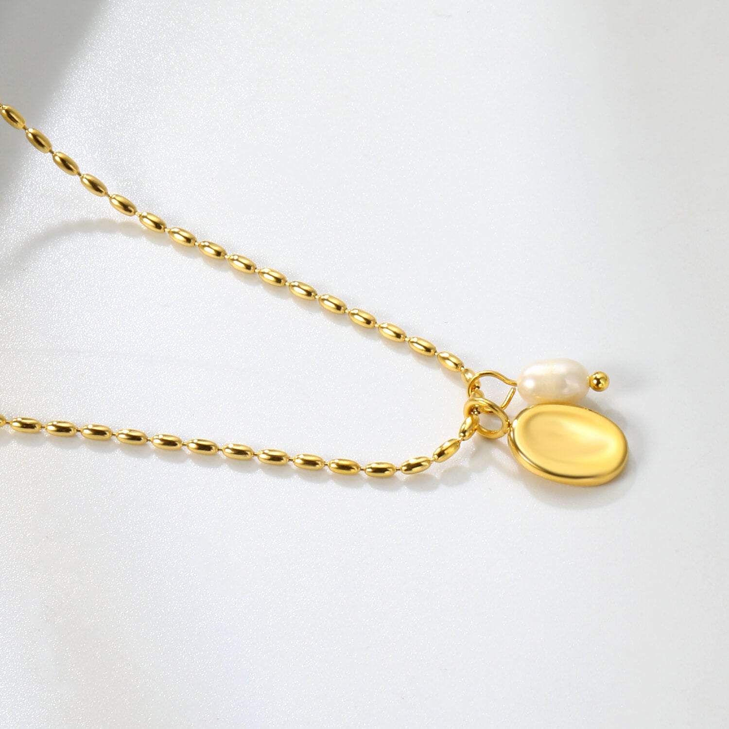 Lähikuva madowwn kullatusta kaulakorusta jossa makeanvedenhelmi