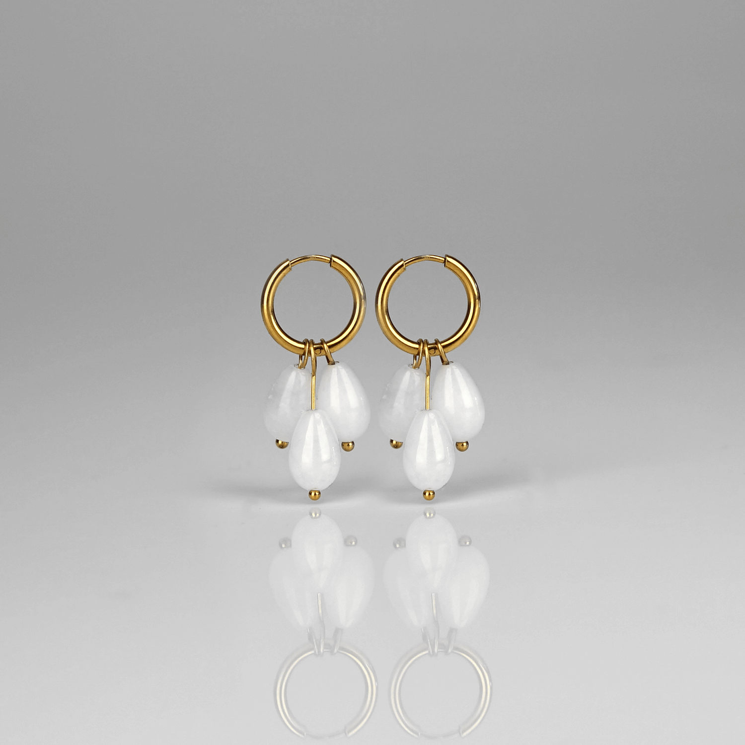 Madowwn Cascade Frost kullatusta ruostumattomasta teräksestä valmistetut korvakorut roikkuvilla valkoisen läpikuultavilla luonnonkivillä valkoista taustaa vasten