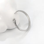 Madoww brändin Cobra vedenkestävä ruostumattomasta teräksestä valmistettu hopean värinen sormus. Sormuksessa on kobran pää ja se nojaa valkoista elementtiä vasten.