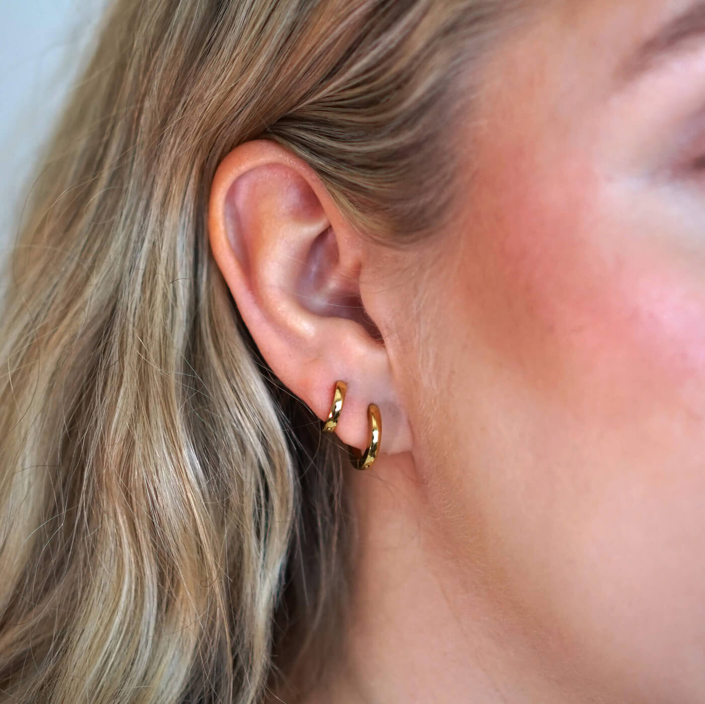 Kullatut huggies korvakorut naisen päällä