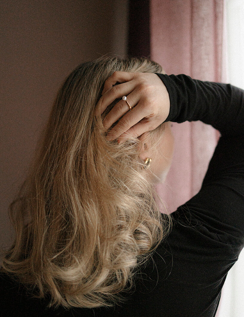 Kullattu sormus helmellä. Nuori nainen jolla Madoww brändin sormus sormessa ja käsi pään päällä.