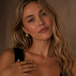 A woman wearing a PVD 18K gold-plated aqua pearl necklace in warm, soft lighting. The delicate gold chain and small aqua pearl pendant stand out in a natural portrait setting.