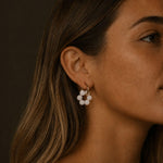 Close-up portrait of a woman wearing gold hoop earrings with translucent milky white stone beads, softly lit against a dark neutral background.