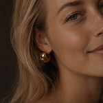 Close-up beauty portrait of a blonde woman with glowing skin wearing a chunky gold hoop earring made from 18k PVD gold-plated stainless steel.