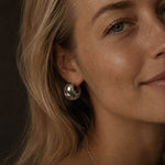 Close-up beauty portrait of a blonde woman with luminous skin wearing a chunky silver-tone hoop earring made from stainless steel, edited to match the same photoshoot style.
