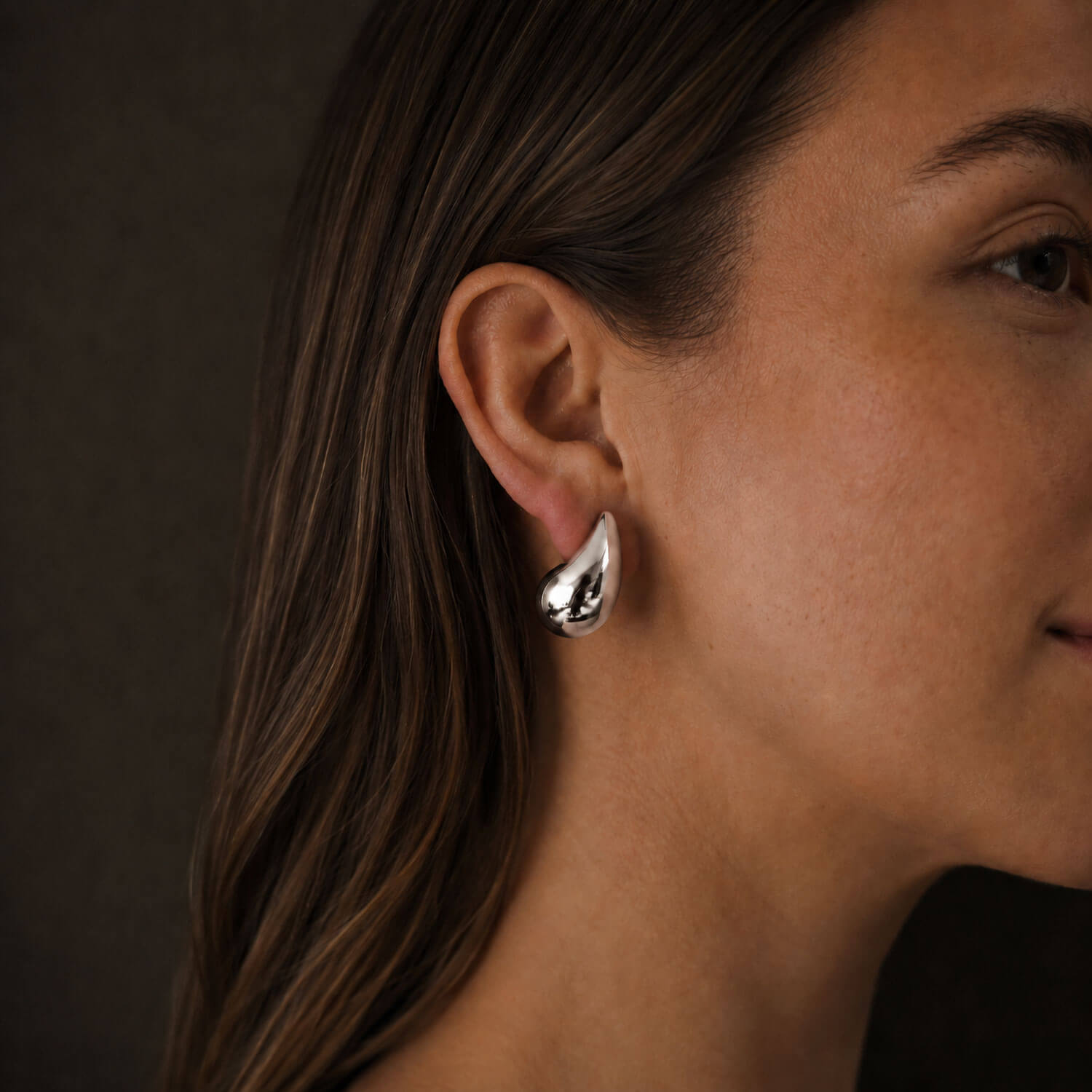 Dew Earring in silver worn on model, close-up side profile with a dark background.