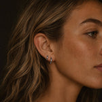 Silver-toned stainless steel huggie earrings worn on a woman’s ear.
