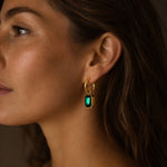 Close-up side profile of a woman wearing an 18k PVD gold-plated stainless steel hoop earring with a large green zircon pendant.